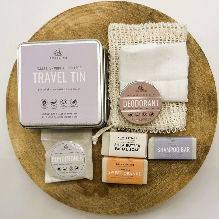 Collection of travel sized natural skincare and hair care products with a travel tin on a wooden board